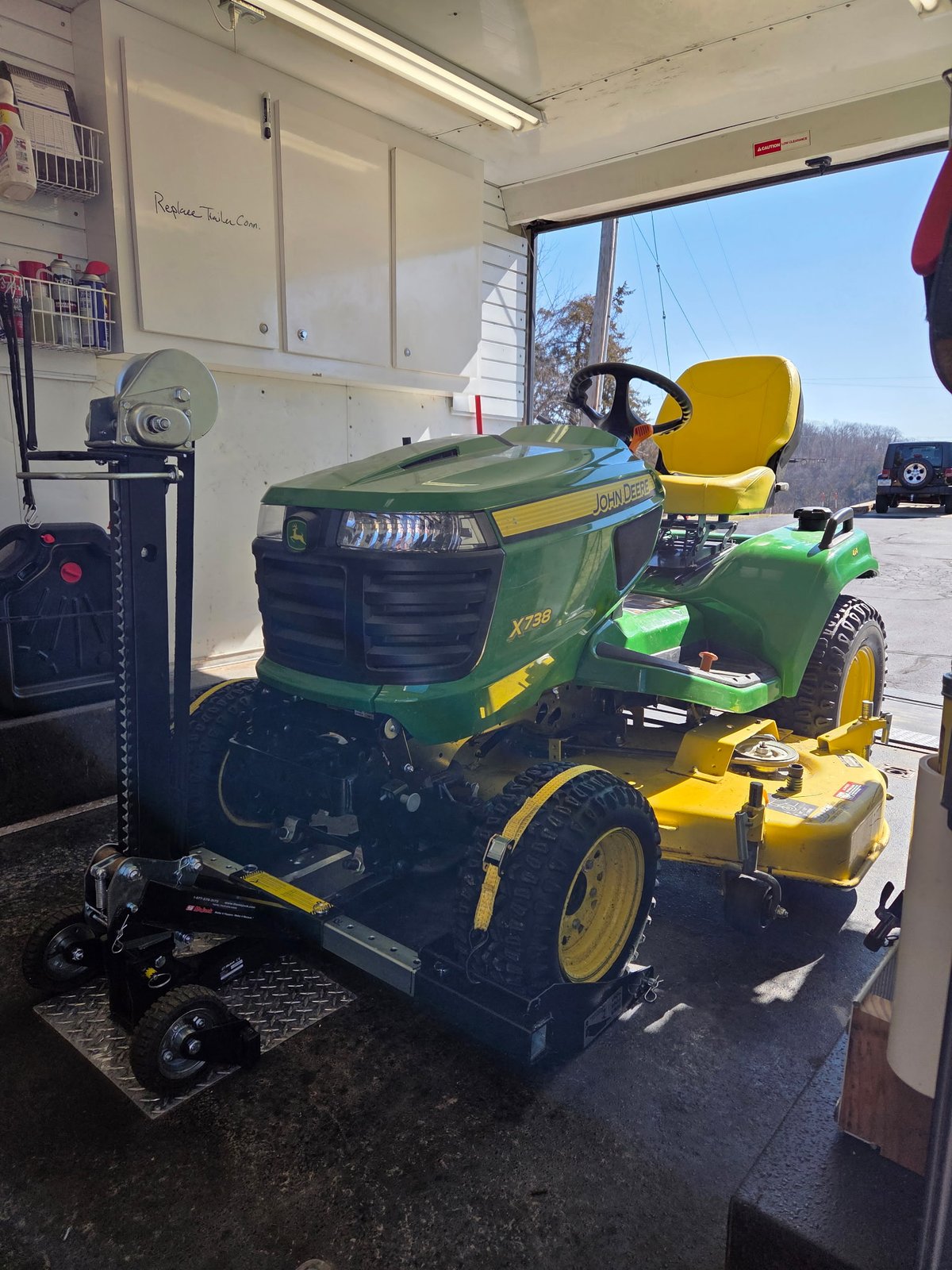 John Deere X738 garden tractor loaded inside the mobile workshop, front view showing the mower deck and headlights