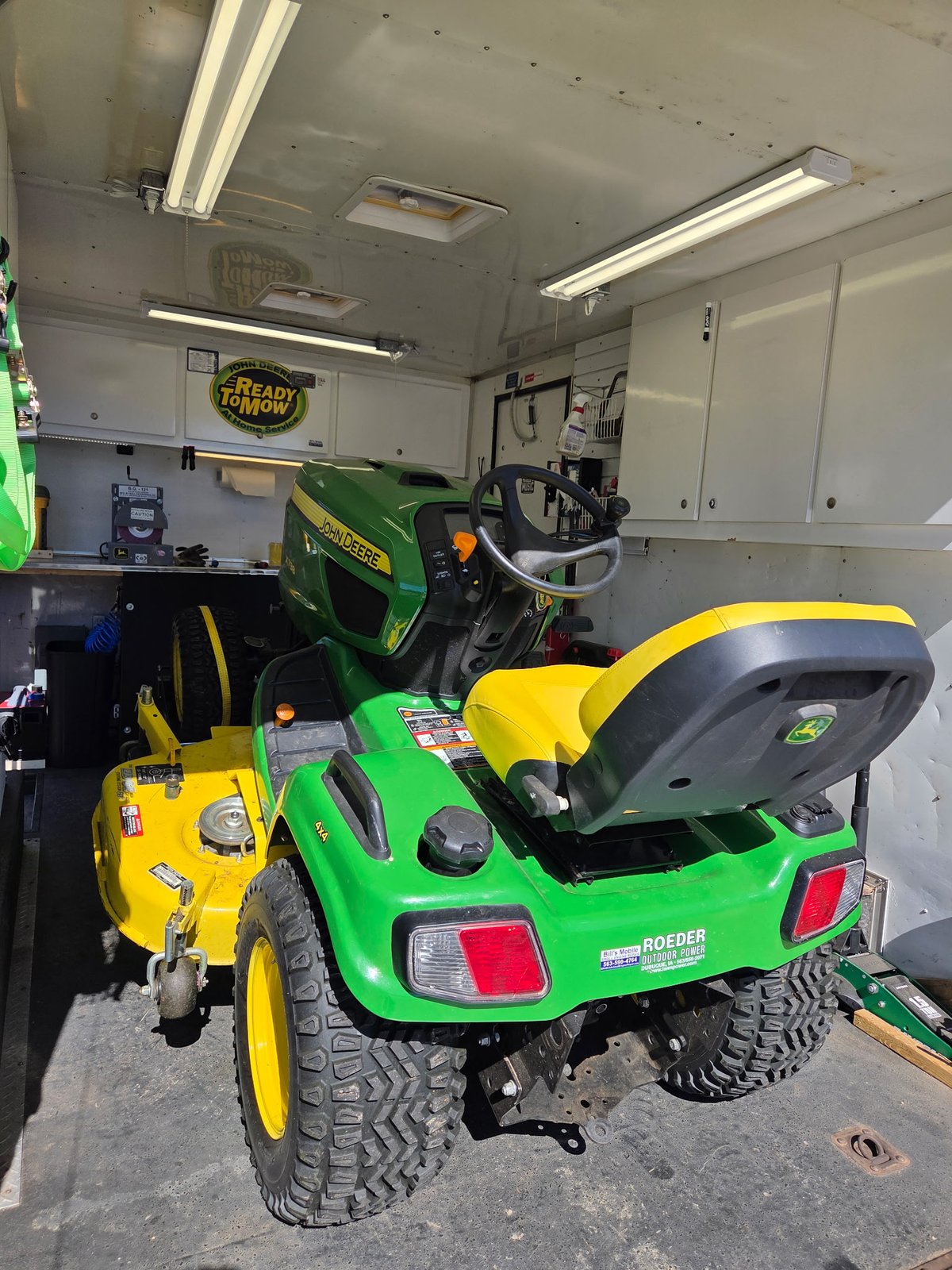John Deere X738 tractor inside the workshop, rear three-quarter view showing Roeder dealer badge and yellow seat