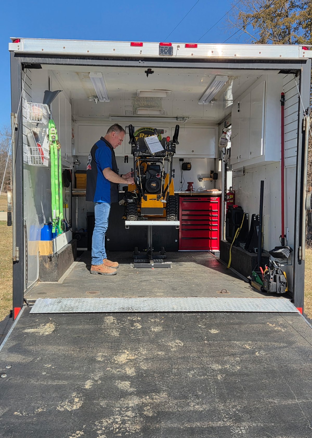 Bill working inside the fully equipped mobile workshop with trailer doors open and a riding mower on the hydraulic lift